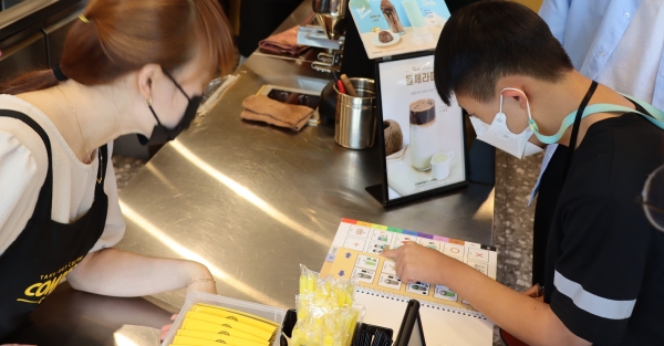 심민건(오른쪽) 군이 지난달 25일 AAC의사소통판을 이용해 커피전문점에서 음료를 구매하고 있는 모습. /주성희 기자