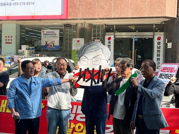 경남정치개혁광장시민연대가 15일 국민의힘 경남도당 앞에서 김미나 창원시의원의 얼굴이 그려진 종이 위에 검은색 테이프를 붙이고 있다. /경남정치개혁광장시민연대
